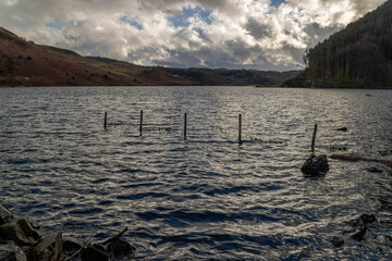 Lake Geirionydd, Snowdonia. Submerged stock fence across the edge of the lake, with mountains behind. Blue sky and fluffy clouds.