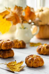 Naklejka na ściany i meble Thanksgiving pumpkin buns. Tasty homemade pumpkin shaped buns on a wooden table with autumnal maple golden leaves. High key, vertical orientation