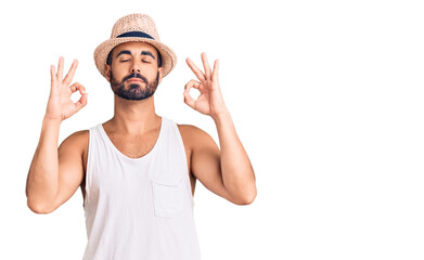 Fototapeta premium Young hispanic man wearing casual summer hat relax and smiling with eyes closed doing meditation gesture with fingers. yoga concept.