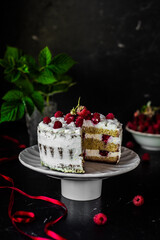 A tasty biscuit sponge cake with cream cheese and fresh raspberries and mint leaves. Sweet dessert with berries on a dark table, low key, negative space, vertical orientation