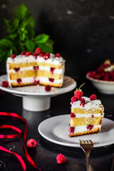 A piece of tasty biscuit sponge cake with cream cheese and fresh raspberries and mint leaves. Sweet dessert with berries on a dark table, low key, negative space, vertical orientation