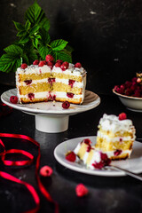 A piece of tasty biscuit sponge cake with cream cheese and fresh raspberries and mint leaves. Sweet dessert with berries on a dark table, low key, negative space, vertical orientation