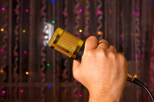 Microphone in hand. Interview. Karaoke. A man's hand holds a microphone against the background of blurry garlands.
