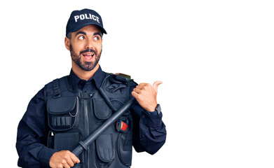 Young hispanic man wearing police uniform holding baton pointing thumb up to the side smiling happy with open mouth