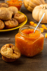 Pumpkin jam. Tasty homemade sweet spicy vegetable jam in a glass jar. Profiteroles and pumpkins background. Vertical orientation