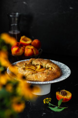 French galette with peaches. Open pie with slices of peach. Fruits and flowers on the table. Vertical orientation.