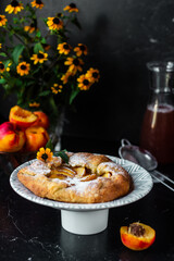 French galette with peaches. Open pie with slices of peach. Fruits and flowers on the table. Vertical orientation.