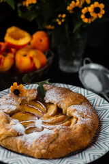 French galette with peaches. Open pie with slices of peach. Fruits and flowers on the table. Vertical orientation.