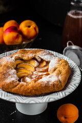 French galette with peaches. Open pie with slices of peach. Fruits and flowers on the table. Vertical orientation.