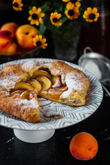 French galette with peaches. Open pie with slices of peach. Fruits and flowers on the table. Vertical orientation.