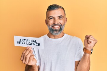 Middle age handsome man holding artificial intelligence word on paper screaming proud, celebrating victory and success very excited with raised arm