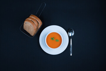 Tomato soup with basil, and bread in a bowl. Dark background.
