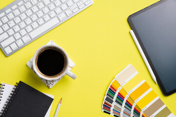 Designer desk top view with computer keyboard, graphic tablet color palette, notebook, cup of coffee on yellow background. Flat lay, view from above. Creative professional workspace.