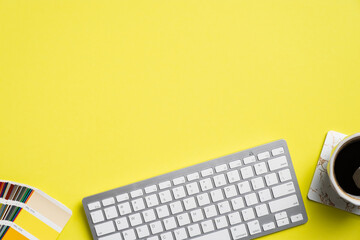 Graphic designer desk top view with computer keyboard, color palette, cup of coffee on yellow...