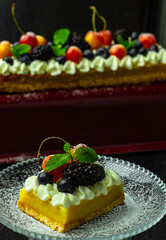 A square piece of tasty lemon curd tart with whipped cream and fresh berries on the top. Sour filling on short crust pastry with blackberries, cherries and fresh mint. Vertical orientation.