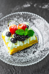 A square piece of tasty lemon curd tart with whipped cream and fresh berries on the top. Sour filling on short crust pastry with blackberries, cherries, blueberries and fresh mint.