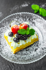 A square piece of tasty lemon curd tart with whipped cream and fresh berries on the top. Sour filling on short crust pastry with blackberries, cherries, blueberries and fresh mint.