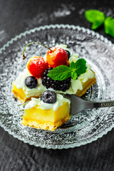 A square piece of tasty lemon curd tart with whipped cream and fresh berries on the top. Sour filling on short crust pastry with blackberries, cherries, blueberries and fresh mint.