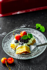 A square piece of tasty lemon curd tart with whipped cream and fresh berries on the top. Sour filling on short crust pastry with blackberries, cherries, blueberries and fresh mint.