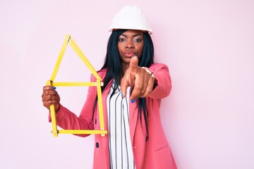 Young african american woman wearing bike helmet and holding water bottle pointing with finger to the camera and to you, confident gesture looking serious