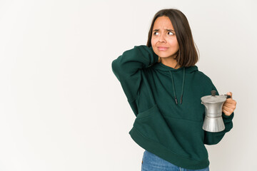 Young hispanic woman holding a coffee maker touching back of head, thinking and making a choice.