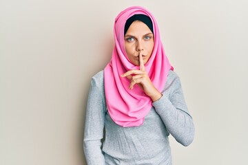 Young caucasian woman wearing traditional islamic hijab scarf asking to be quiet with finger on lips. silence and secret concept.