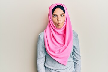 Young caucasian woman wearing traditional islamic hijab scarf making fish face with lips, crazy and comical gesture. funny expression.