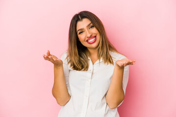 Young indian woman isolated on pink background holding something with palms, offering to camera.