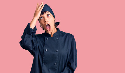 Young brunette woman with short hair wearing professional cook uniform surprised with hand on head for mistake, remember error. forgot, bad memory concept.