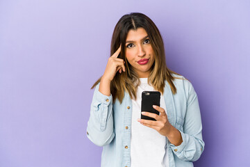 Fototapeta premium Young indian woman holding a phone isolated pointing temple with finger, thinking, focused on a task.