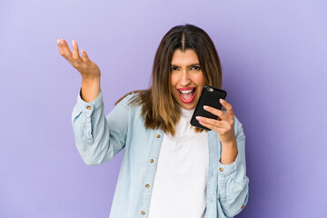 Young indian woman holding a phone isolated receiving a pleasant surprise, excited and raising hands.