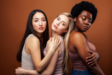 young pretty asian, caucasian, afro woman posing cheerful together on brown background, lifestyle diverse nationality people concept