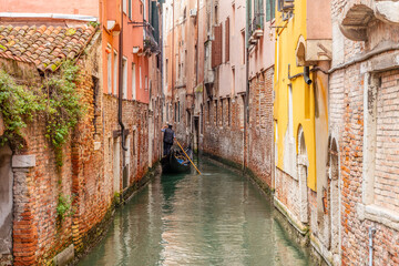 Obraz na płótnie Canvas Venetian gondolier punting gondola through green canal waters of Venice Italy