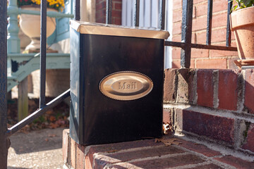 Close up isolated image of a small size vertical mail box that is attached to the railings of the brick outdoor stairs at the entrance of a townhome. This parcel box has a secure locking mechanism.