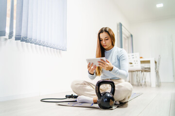 Front view on young caucasian woman sitting on the floor at home watching online video for training - Girl with digital tablet looking for workout on internet - health and fitness concept copy space