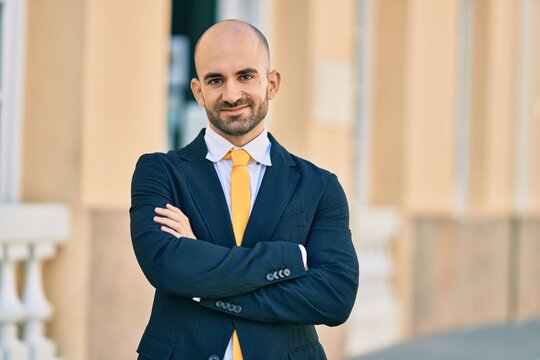 Young hispanic bald businessman with arms crossed smiling happy at the city.
