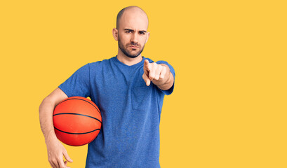Young handsome man holding basketball ball pointing with finger to the camera and to you, confident...