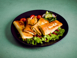 Salty pancakes with salad and other garnishes in a black plate on a rustic green background