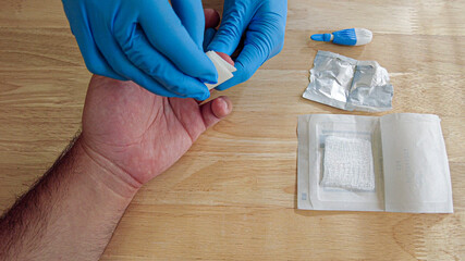 A medical personnel wearing gloves is wiping the finger tip of a patient with a sterile alcohol wipe before performing a finger prick blood draw for a diagnostic test at a doctor's office