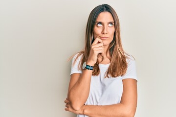 Brunette young woman wearing casual white t shirt thinking concentrated about doubt with finger on...