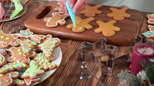 A female hand paints with colored sugar icing on Christmas gingerbread men