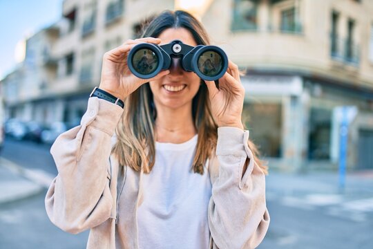 Young caucasian woman smiling happy looking for new opportunity using binoculars walking at the city.