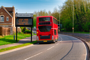 Traffic information sign in England during Covid 19 pandemic with red double-decker bus passing by