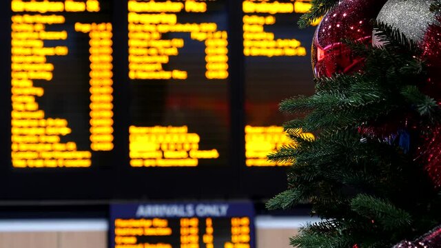 Abstract travel at Christmas - New Year festive period concept shot showing red Christmas tree decoration bauble against blurred arrival departure display board at a train station.