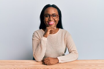 Young african woman wearing casual clothes sitting on the table smiling looking confident at the...