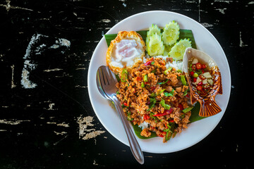 Thai food fried rice with pork basil placed in a white plate placed on a black wooden table.