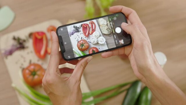 Top view food photo. Hands woman taking a picture of board with vegetables on wooden table. Vegan blogging lunch blogger. Slow motion