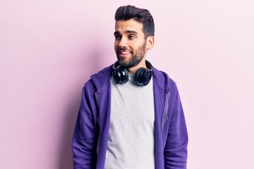 Young handsome man with beard listening to music using headphones looking to side, relax profile pose with natural face and confident smile.