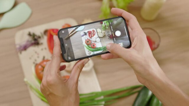 Young woman hands taking a picture of board with vegetables on wooden table. Top view food photo. Touch zoom. Vegan blogging lunch blogger. Slow motion