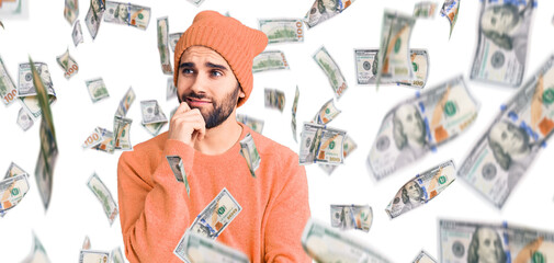 Young handsome man with beard wearing casual sweater and wool cap serious face thinking about question with hand on chin, thoughtful about confusing idea